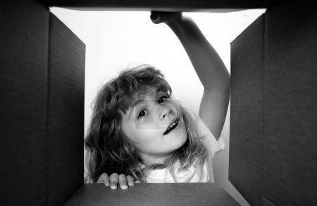 Foto de Niño desempacar y abrir la caja de cartón, y mirando hacia el interior con la cara sorpresa. Desembalaje caja de cartón para niños - Imagen libre de derechos