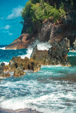 Téléchargez les photos : Les vagues de l'océan s'écrasent sur la côte de l'île rocheuse. Des vagues et des pierres océaniques éclaboussantes. Plage de sable rouge, Maui en hawaïen - en image libre de droit