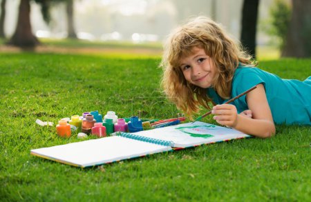 Téléchargez les photos : Enfants peignant dans la nature printanière. Enfant garçon appréciant l'art et l'artisanat dessin dans la cour arrière ou parc de printemps. Dessin pour enfants avec crayons en plein air - en image libre de droit