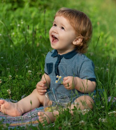 Foto de Bebé niño en la hierba en el fieald en verano. Lindo niño emocionado sentado al aire libre - Imagen libre de derechos