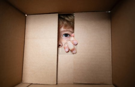 Excited child boy looking into the box, shipping cardboard box. Close up eyes looking. Parcel packaging or unpacking concept