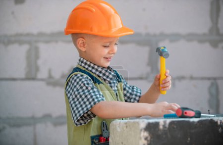 Foto de Niño pequeño en casco protector naranja con instrumentos para la renovación. Reparación casa - Imagen libre de derechos
