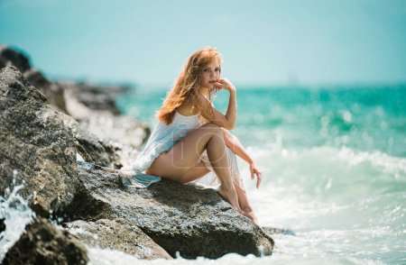 Photo for Young sensual woman sitting on the beach. Woman relax sitting near water at sea, enjoy holidays and weekend vacation in summer time - Royalty Free Image