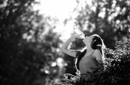 Téléchargez les photos : Femme saine buvant de l'eau de bouteille dans la forêt. Restez hydratation concept. Non cachée. Unité avec la nature, extérieur - en image libre de droit