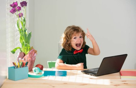Foto de El chico de la escuela haciendo la tarea. Sorprendido niño aprende con el ordenador portátil en la sala de estudio - Imagen libre de derechos