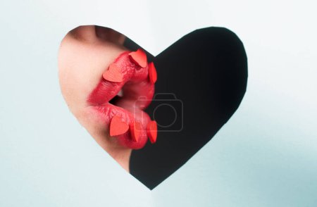 Téléchargez les photos : J'adore les lèvres rouges. Lèvres avec des cœurs à travers le papier. Maquillage des coeurs. Concept d'amour - en image libre de droit