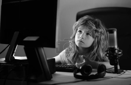 Téléchargez les photos : Petit gamer enfant jouer jeu d'ordinateur sur le bureau. Flux de jeu et blogging pour les enfants. Enfant utilisant l'informatique à la maison - en image libre de droit