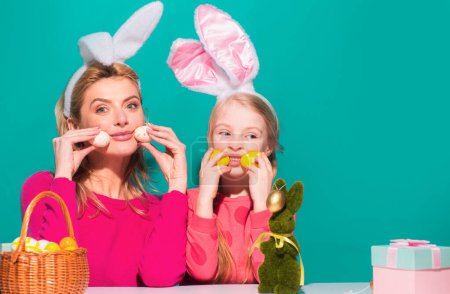 Téléchargez les photos : Mère et fille dans les oreilles de lapin sur Pâques Holding oeufs, isolé sur bleu - en image libre de droit