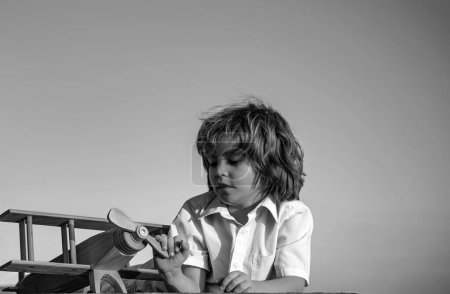 Foto de Niño jugando con un avión de juguete de madera, sueña con convertirse en piloto. Sueños de niños. Aviador piloto infantil con avión de madera - Imagen libre de derechos