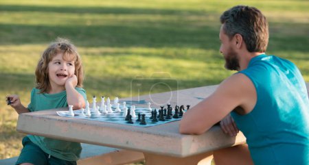 Téléchargez les photos : Joyeux famille en plein air. Père et fils jouent aux échecs dans le jardin d'été. Jeux et activités pour enfants - en image libre de droit