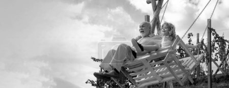 Photo for Old grandfather and young child grandson swinging in garden outdoors. Grand dad and grandson sitting on swing in park. Grandfather and grandchild, spring banner - Royalty Free Image