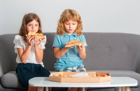 Photo for Pizza and kids, slices pizza in kids hand. Children eating tasty fast food pizza with cheese. Happy time for hungry friends children in family. Two kids bite pizza indoors - Royalty Free Image