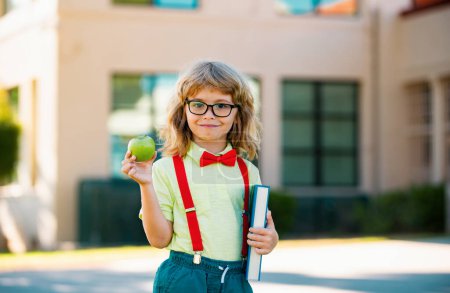 Photo for Smiling little student boy wearing school backpack and holding exercise book. Portrait of happy pupil outside the primary school. Closeup face of smiling hispanic schoolboy looking at camera - Royalty Free Image