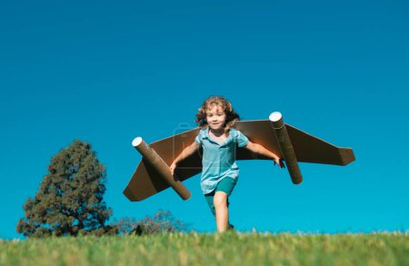 Téléchargez les photos : Enfant garçon avec des ailes au ciel imagine un pilote et rêve de voler. Aventure enfant, concept de liberté et d'imagination enfant - en image libre de droit