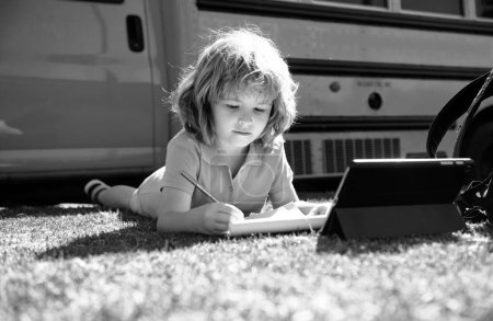 Photo for Portrait of little schoolboy writing outdoor in schoolyard park and doing homework - Royalty Free Image
