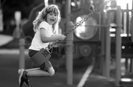 Foto de Child playing on outdoor playground. Kids play on kindergarten yard. Kid boy having fun on outdoor playground. Colorful playground with a swing, slide, climbing ladder - Imagen libre de derechos