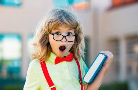 Foto de Un chico de la escuela primaria. El chico feliz con gafas va a la escuela por primera vez. Niño con mochila y libro. Regreso a la escuela - Imagen libre de derechos