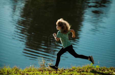 Foto de Un chico corriendo en el lago. Niño feliz correr en el lago en las vacaciones de verano. Deportivo niño pequeño trotar y entrenar al aire libre - Imagen libre de derechos
