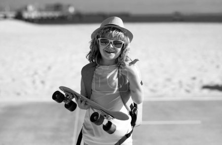 Photo for Childhood. Cute child with skateboard on street background. Funny kid boy, stylish skater holding skateboard outdoor. Amazed child with thumb up, street portrait - Royalty Free Image