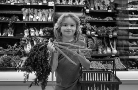 Foto de Niño con zanahoria. Niño comprando fruta en el supermercado. El niño compra verduras frescas en la tienda de comestibles. Niño eligiendo verduras. Alimento saludable - Imagen libre de derechos