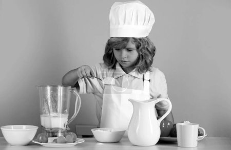 Téléchargez les photos : Petit garçon en chapeau de chef et tablier préparant le repas. Petit cuisinier avec des légumes à la cuisine. Alimentation naturelle pour enfants - en image libre de droit