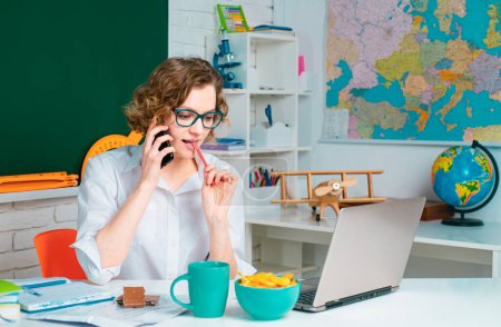 Photo for Learn with fun. Funny female teacher with mobile phone use laptop, sitting at her workplace and teaching English. Education concept - Royalty Free Image