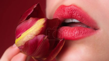 Téléchargez les photos : Rouge à lèvres rouge. Tulipe de tendresse. Lèvres naturelles tendres avec tulipes. Sensibilité femme sexy bouche. Soin et tendresse. Gros plan belles lèvres tendres avec des fleurs de tulipes. Touche de tendresse - en image libre de droit