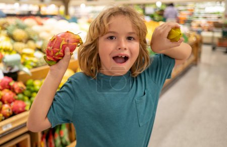 Téléchargez les photos : Enfant avec des fruits. Portrait d'enfant dans un magasin d'alimentation ou un supermarché. Un gamin qui va faire du shopping. Aliments sains pour enfants - en image libre de droit