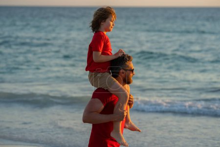 Photo for Father and son boy walking on beach. Summer holiday. Father and son enjoying summer vacation together. Father and son playing on beach. Son on fathers shoulders piggyback ride - Royalty Free Image
