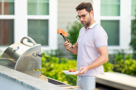 Photo for Handsome man preparing barbecue salmon. Male cook cooking meat on barbecue grill. Guy cooking salmon on barbecue for summer family dinner at the backyard of the house - Royalty Free Image