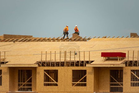 Téléchargez les photos : Toiture sur le toit. Constructeur toiture installer un nouveau toit. Toiture d'un travailleur de la construction sur un grand immeuble d'appartements sur le toit. Charpentier de toiture travaillant sur le chantier de construction de la structure du toit - en image libre de droit