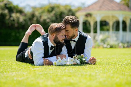 Photo for Gay couple laying on grass on wedding day. Gay marriage. Gay couple wedding. Homosexual couple celebrating wedding, LBGT couple at wedding ceremony, LGBTQ - Royalty Free Image