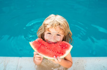 Téléchargez les photos : Un drôle d'enfant joue dans la piscine. L'enfant mange une pastèque sucrée, profiter de l'été. Enfance insouciante - en image libre de droit