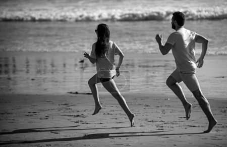 Téléchargez les photos : Sportsman et sportive qui courent ensemble au bord de la mer. Couple courant sur la plage - en image libre de droit