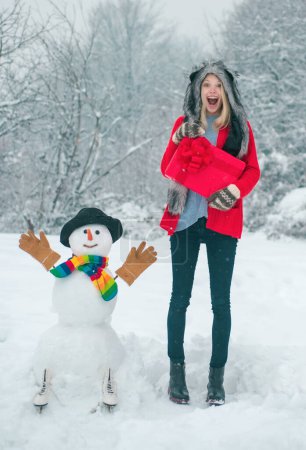 Téléchargez les photos : Joyeuse fille s'amuser avec bonhomme de neige dans Winter Park. Fond d'hiver avec flocons de neige et bonhomme de neige - en image libre de droit