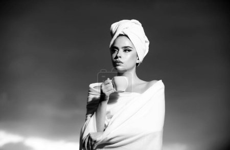 Téléchargez les photos : Une jeune fille boit du café. Femme détendue avec serviette sur la tête sentant le café dans la nuit au ciel dramatique en plein air - en image libre de droit