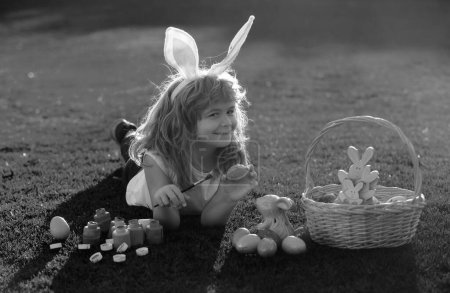 Téléchargez les photos : Enfant avec des œufs de Pâques et des oreilles de lapin posées sur l'herbe. Drôle de garçon, lapin de Pâques enfants - en image libre de droit