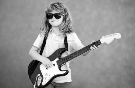 Photo for Funny child with blonde curly hair playing guitar on beige yellow background. Boy guitarist - Royalty Free Image