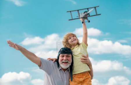 Téléchargez les photos : Enfant garçon et grand-père jouant avec un avion jouet sur fond de ciel d'été. Week-end avec grand-père - en image libre de droit