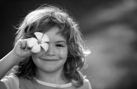 Téléchargez les photos : Gros plan portrait d'un petit garçon blond yeux plumeria fleur. Les enfants drôles dans le parc naturel d'été. Vacances d'été. Couvre les yeux avec le concept de fleur - en image libre de droit