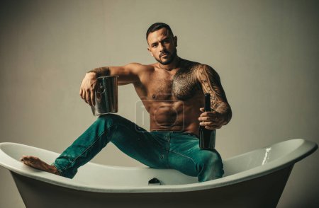 Foto de Sexy hombre musculoso seductor sentarse en la bañera, los hombres de vacaciones con champán. Celebrando Navidad o cumpleaños. Fiesta de sexo privado - Imagen libre de derechos