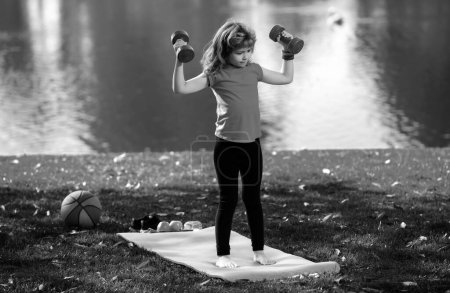 Photo for Funny child lifting the dumbbells in backyard outside. Kids in training - Royalty Free Image