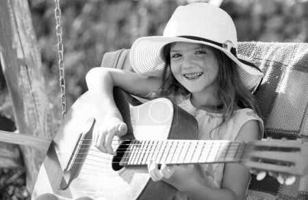 Photo for Little girl musician playing guitar. Summer activity for children in warm weather. Cute little girl having fun on a swing in beautiful summer garden and sunny day outdoors - Royalty Free Image