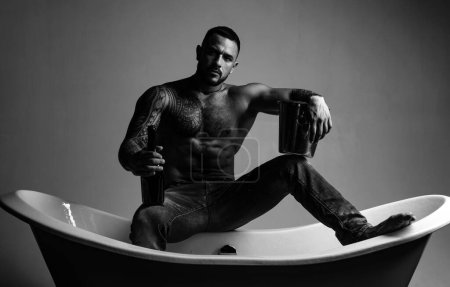 Photo for Sexy seductive muscular man sit on bathtub in bathroom, men holiday with champagne. Celebrating christmas or birthday. Private sex party - Royalty Free Image
