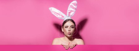 Photo for Easter banner with bunny woman. Close-up portrait of attractive cheerful girl wearing pink ears, air kiss. Easter bunny woman - Royalty Free Image