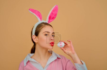 Foto de Los labios y la Pascua, lápiz labial beso huella en huevo de Pascua. Feliz Pascua. Mujer joven con orejas de conejo. Retrato de una mujer feliz con orejas de conejo. Caza de huevos - Imagen libre de derechos