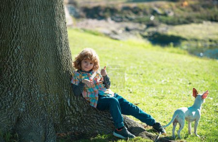 Téléchargez les photos : Enfant drôle avec chien marchant à la pelouse de printemps dans le parc en plein air. Assurance enfants. Joli petit garçon mignon enfant, jouer et s'amuser sur la pelouse d'herbe verte dans le parc. Famille, parentalité, concept d'enfance - en image libre de droit