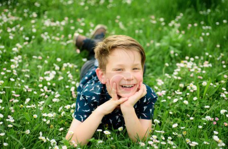 Smiling boy lying on carefree flower field. Cute kid child enjoying on field and dreaming