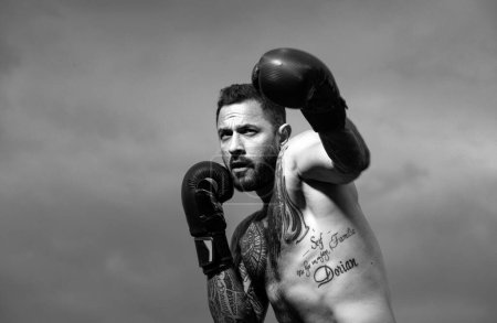 Photo for Boxer in a fight. Fist fight. Strong man with tattooed body boxing outdoor. Man with muscular body and bare torso with boxing punch gloves. Sexy boxing man - Royalty Free Image
