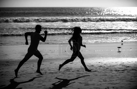 Téléchargez les photos : Sport et mode de vie sain, amis jogging au coucher du soleil sur la plage. Couple silhouette courant sur la plage - en image libre de droit